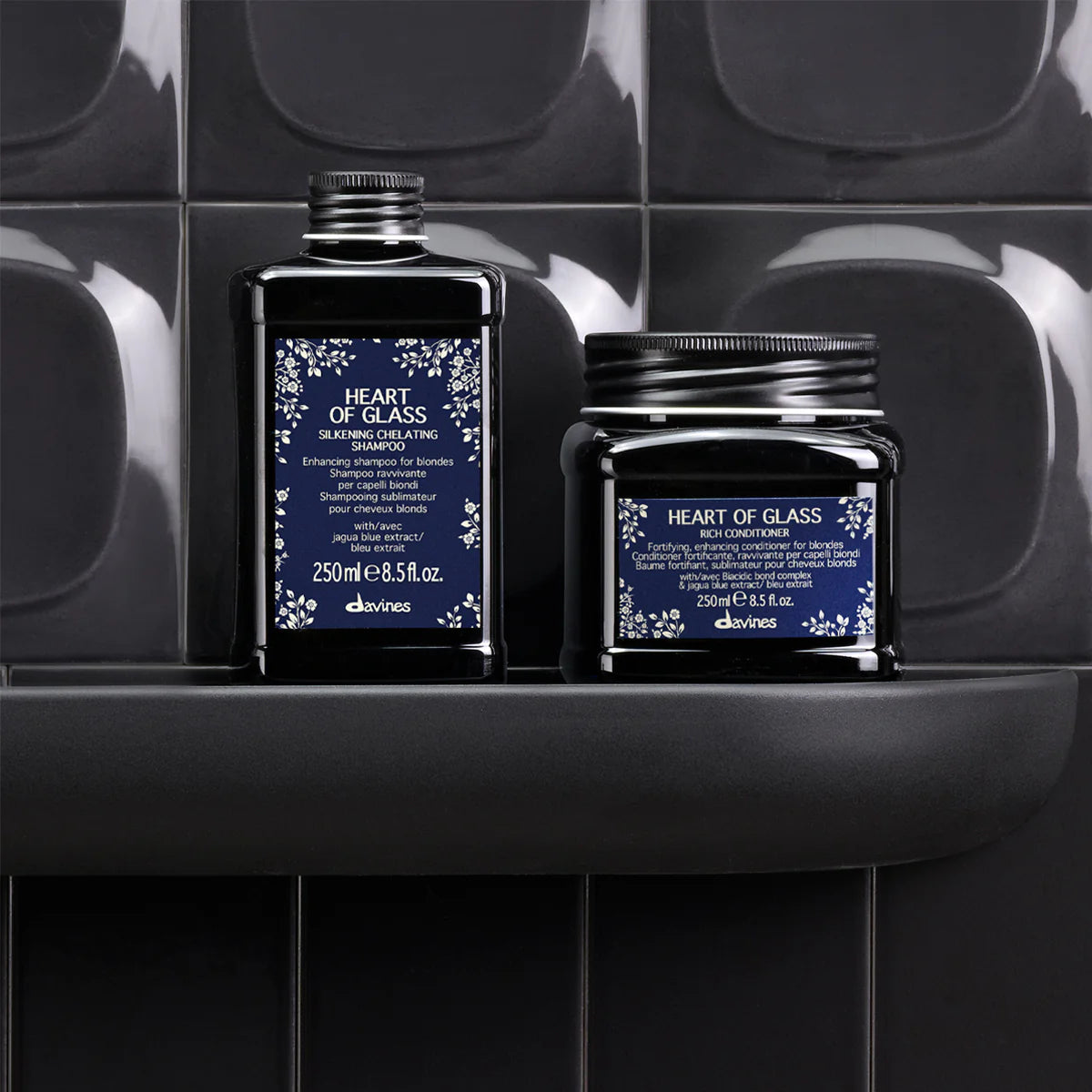 Heart of Glass Rich Conditioner bredvid en matchande hårvårdsprodukt i svarta förpackningar med elegant blå etikett, placerade på en svart hylla mot mörka kakelväggar.