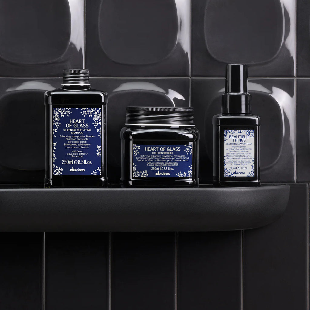 Heart of Glass Silkening Shampoo tillsammans med kompletterande hårvårdsprodukter i svarta förpackningar placerade på en svart hylla mot mörka kakelväggar, miljövänliga hårvårdsprodukter för vård och styling.