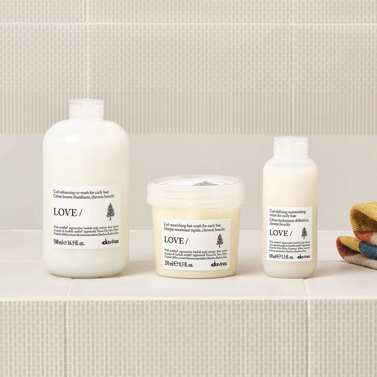 Love Curl Enhancing Fast Mask i mitten av bilden, omgiven av andra hårvårdsprodukter för lockigt hår, på beige hylla med diskret mönster, miljövänlig hårinpackning.