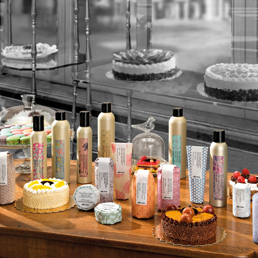 This is a Dry Wax Finishing Spray i en samling av miljövänliga hårvårdsprodukter från Davines, presenterad på ett bord tillsammans med bakverk.