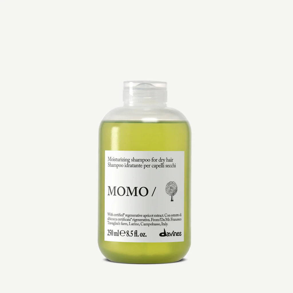 Flaska med Momo Moisturizing Shampoo, ett milt schampo som återfuktar och vårdar torrt hår, i en transparent behållare med grön vätska.
