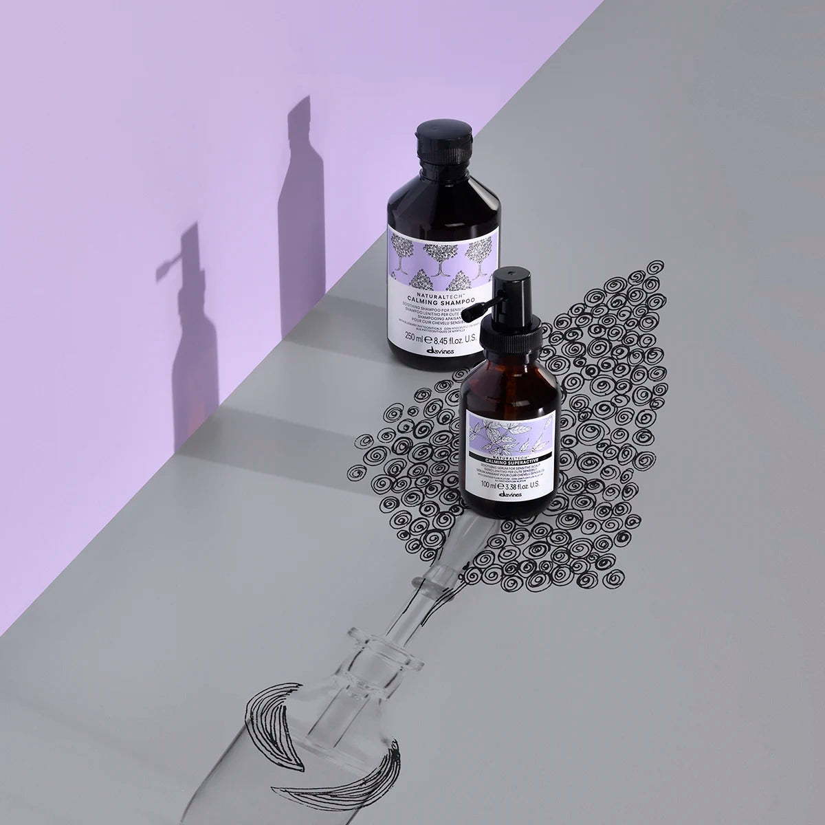 Två flaskor Naturaltech Calming Superactive med lila etiketter står på en yta med en tecknad skiss av hårborste och lockar, en lugnande hårvårdsprodukt från Davines.