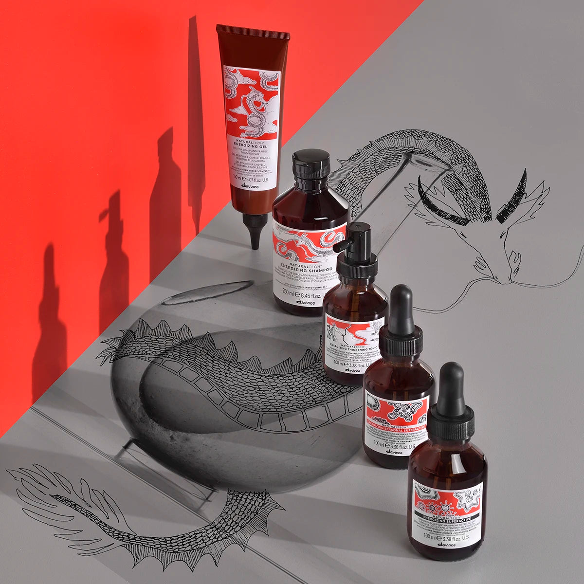 Naturaltech Energizing Gel i brun flaska med pipett placerad bland andra hårvårdsprodukter på en yta med grafisk drakillustration mot röda och gråa bakgrunder.