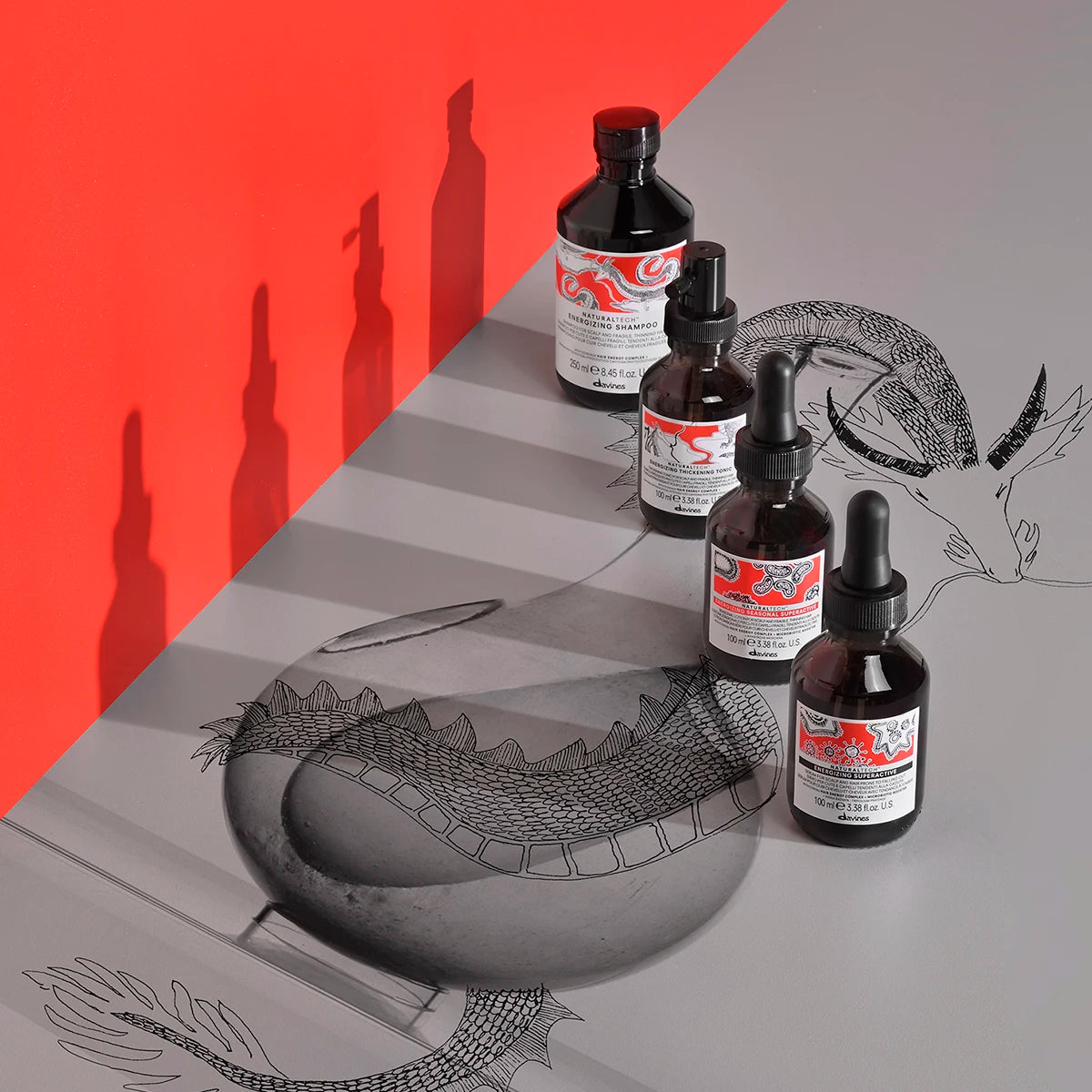 Fyra flaskor med Naturaltech Energizing Seasonal Superactive placerade på en grå yta med svart-röda etiketter och skuggor mot en röd vägg, dekorativa teckningar i bakgrunden.