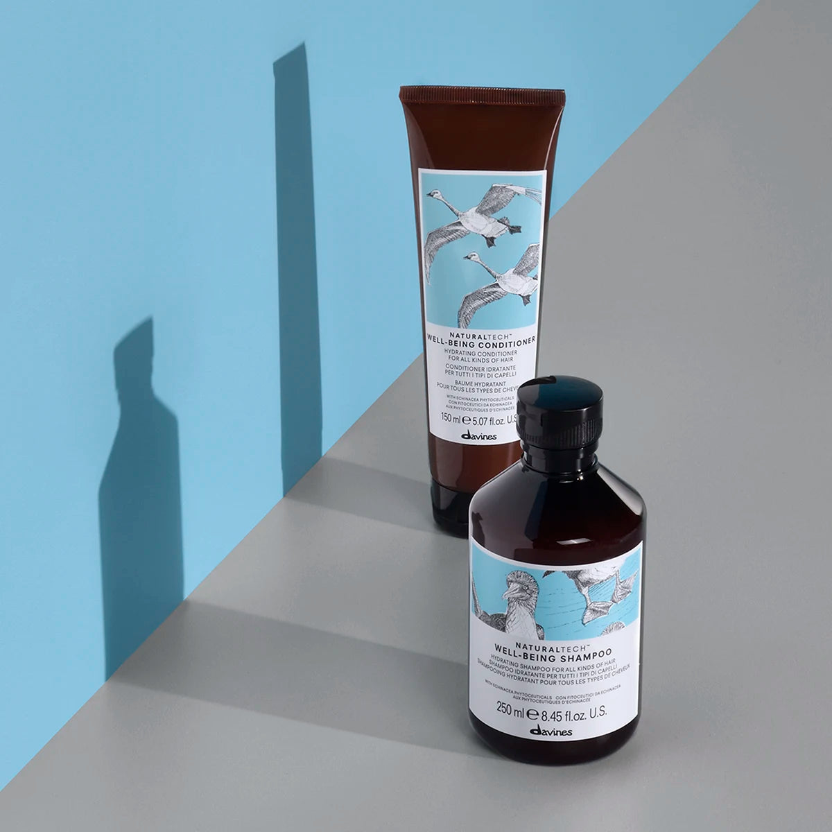 Flaska och tub med Naturaltech Well-Being Shampoo och balsam på grå och blå bakgrund, miljövänliga hårvårdsprodukter från Davines.