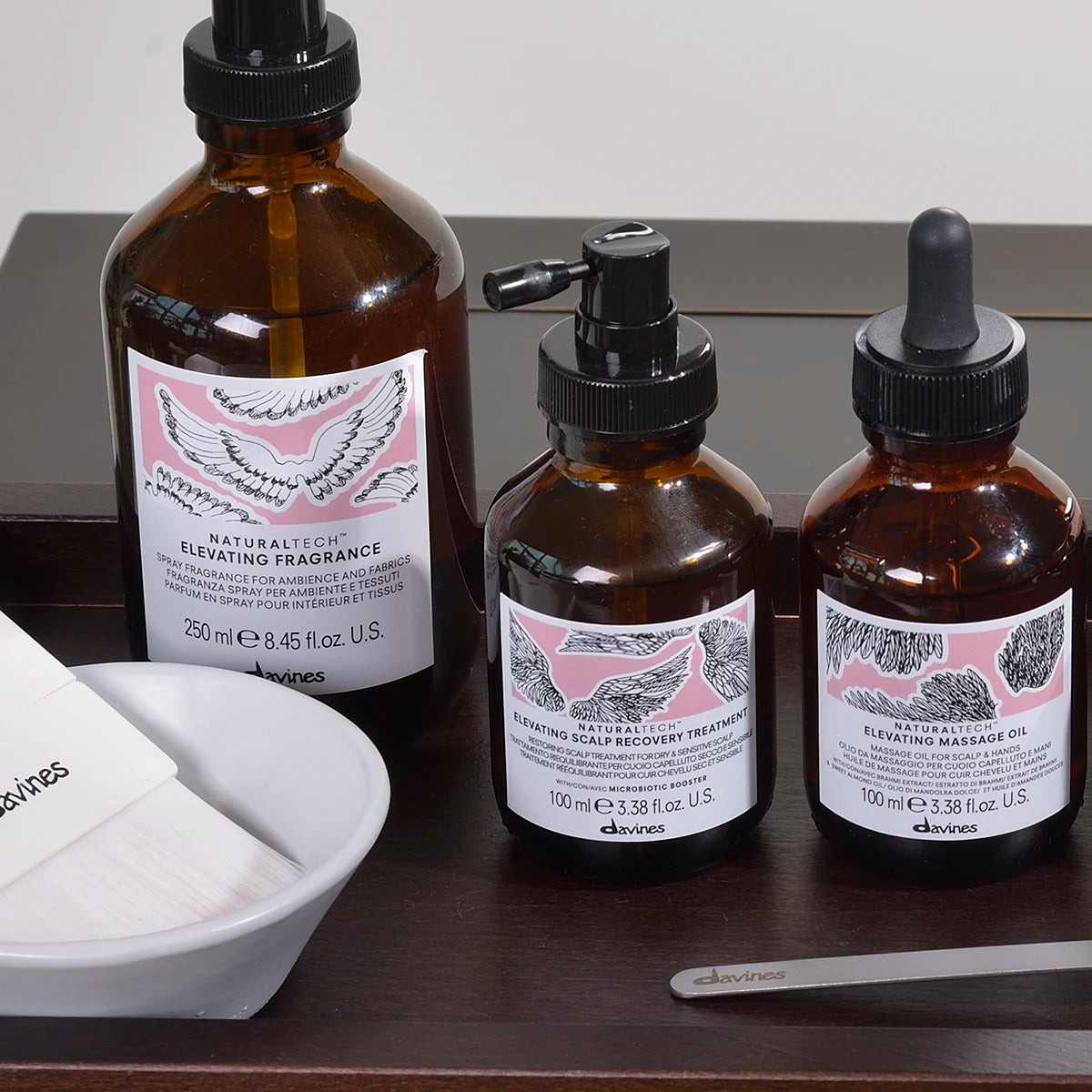 Tre bruna flaskor med pipett och pump med Naturaltech Elevating Scalp Recovery Treatment placerade på ett bord tillsammans med en vit skål och en metallpinne.
