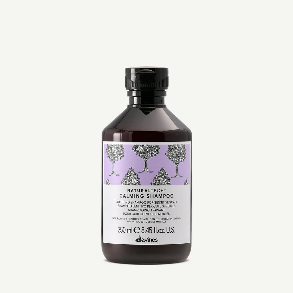 Flaska med Naturaltech Calming Shampoo, ett milt schampo för känslig hårbotten med lugnande egenskaper och en diskret lila etikett med trädillustrationer.