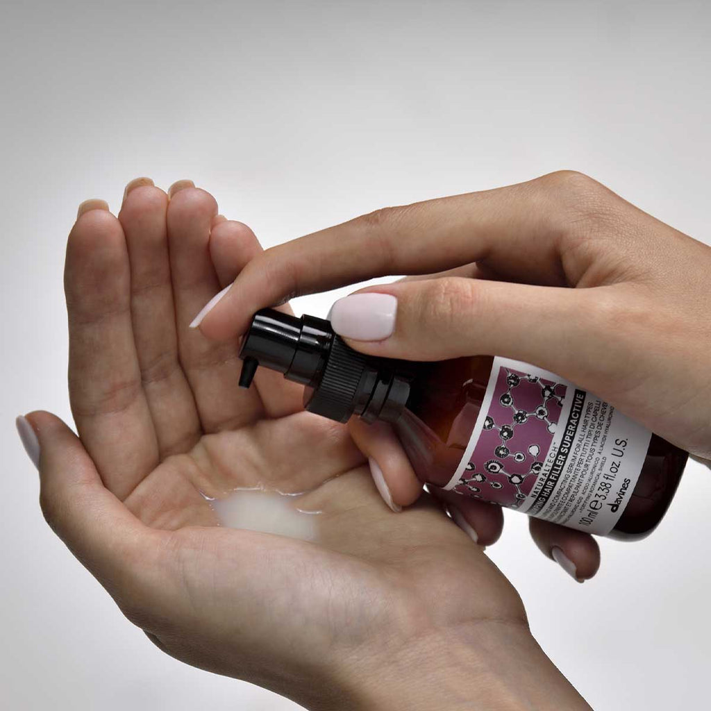 En person som pumpar ut Naturaltech Replumping Hair Filler i handen, en mjölkvit hårbehandling för volym och vård i ett miljövänligt hårvårdssortiment.