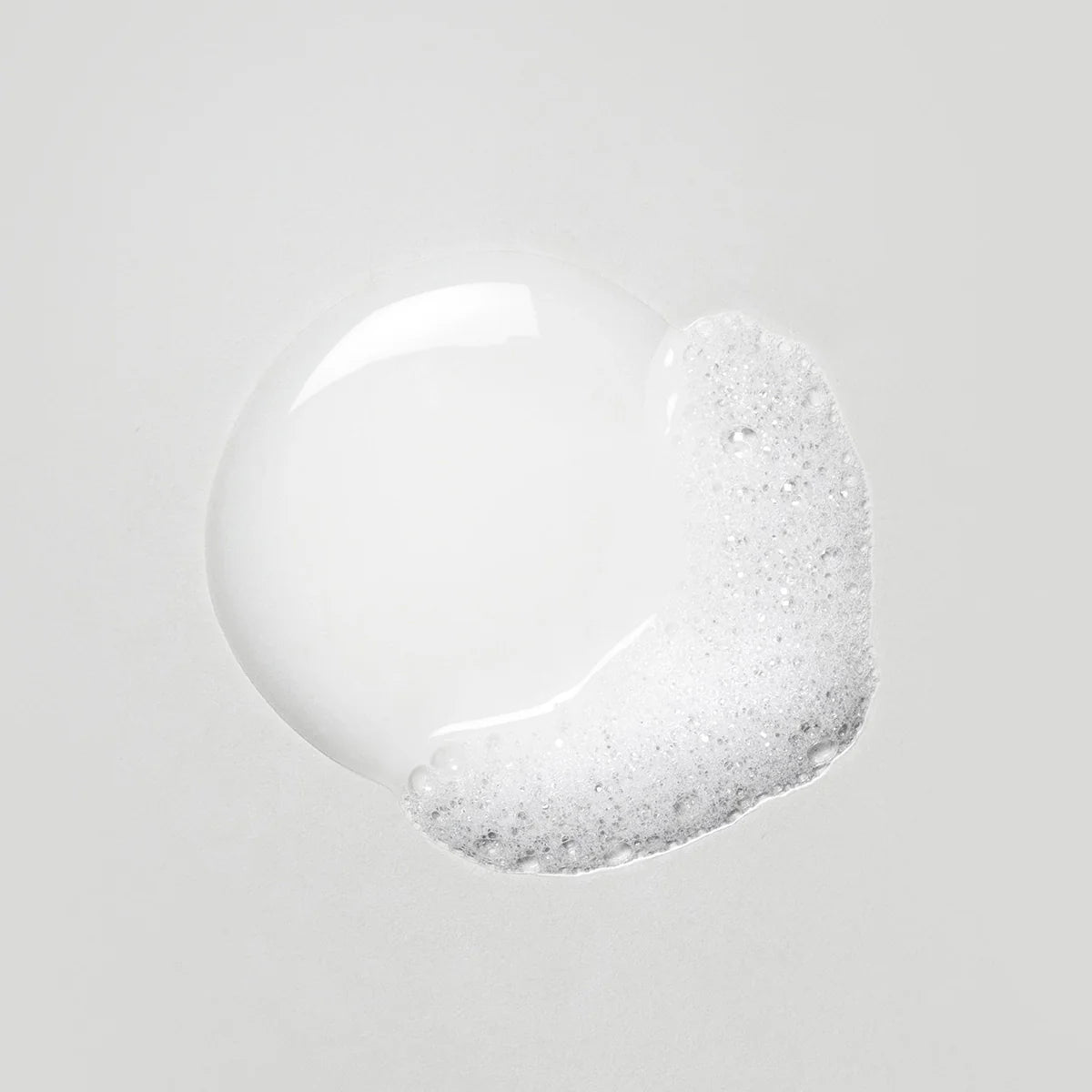 En nära bild av transparent och skummande textur från OI/Body Wash, som visar produktens milt rengörande egenskaper och lätta konsistens.