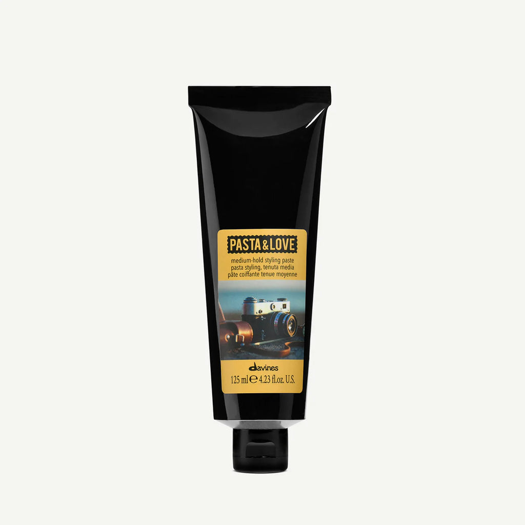 Tub i svart med etikett som visar vintagekamera, innehållande Pasta & Love Medium Hold Styling Paste för medium stadga i håret, 125 ml.