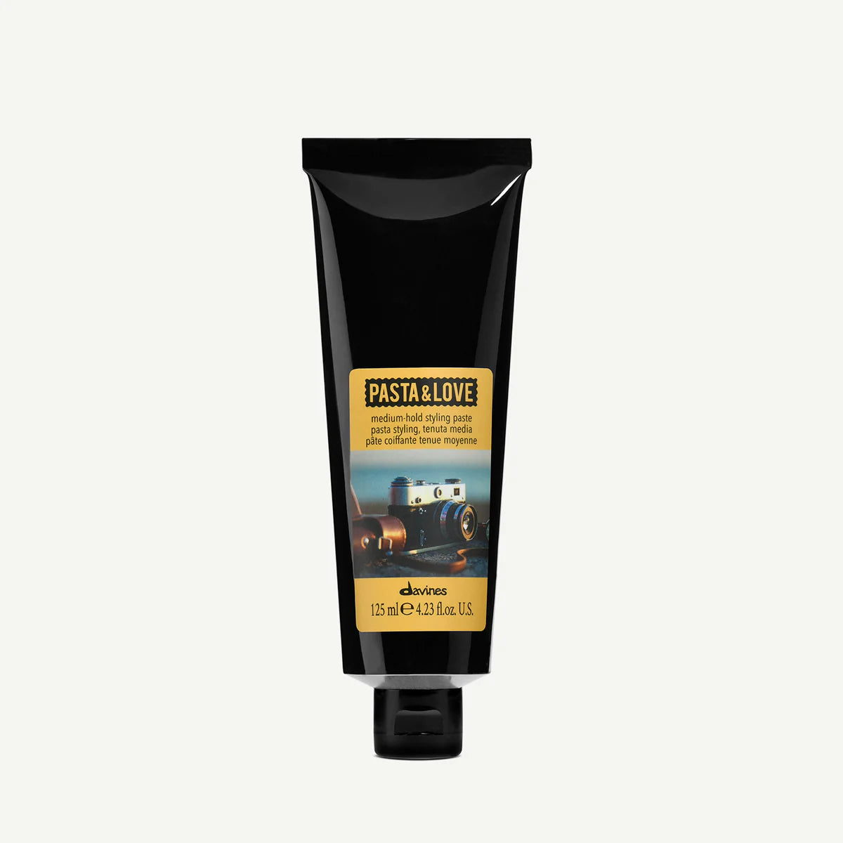 Tub i svart med etikett som visar vintagekamera, innehållande Pasta & Love Medium Hold Styling Paste för medium stadga i håret, 125 ml.