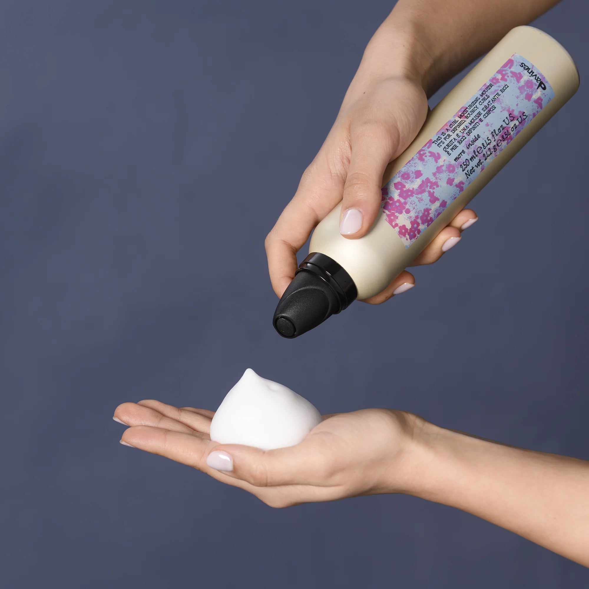 Person som trycker ut skum från en flaska med This is a Curl Moisturizing Mousse för hårstyling och vård.