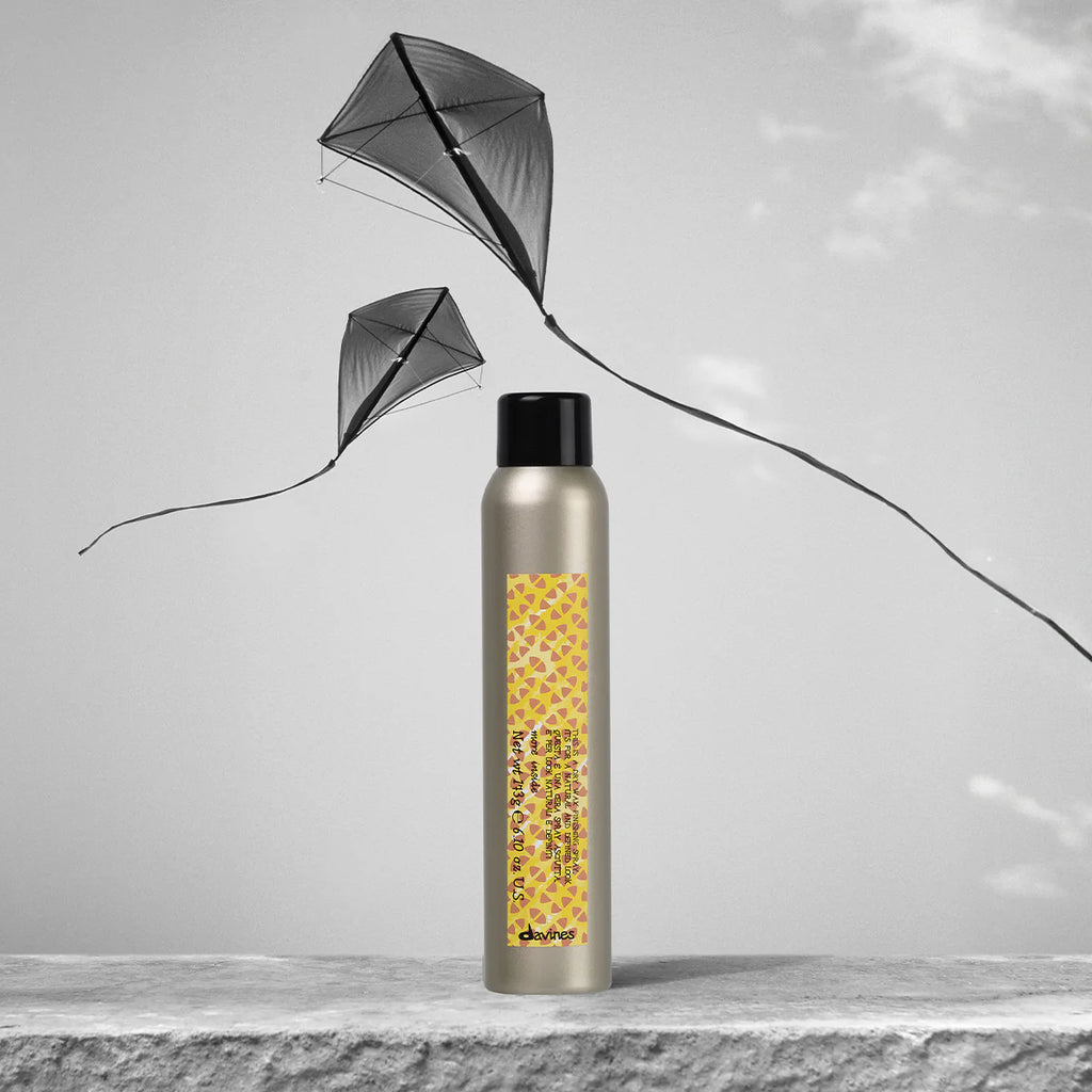 This is a Dry Wax Finishing Spray i en elegant, miljövänlig förpackning framför en grå bakgrund med svävande drakar, perfekt för styling och finish med vaxeffekt.