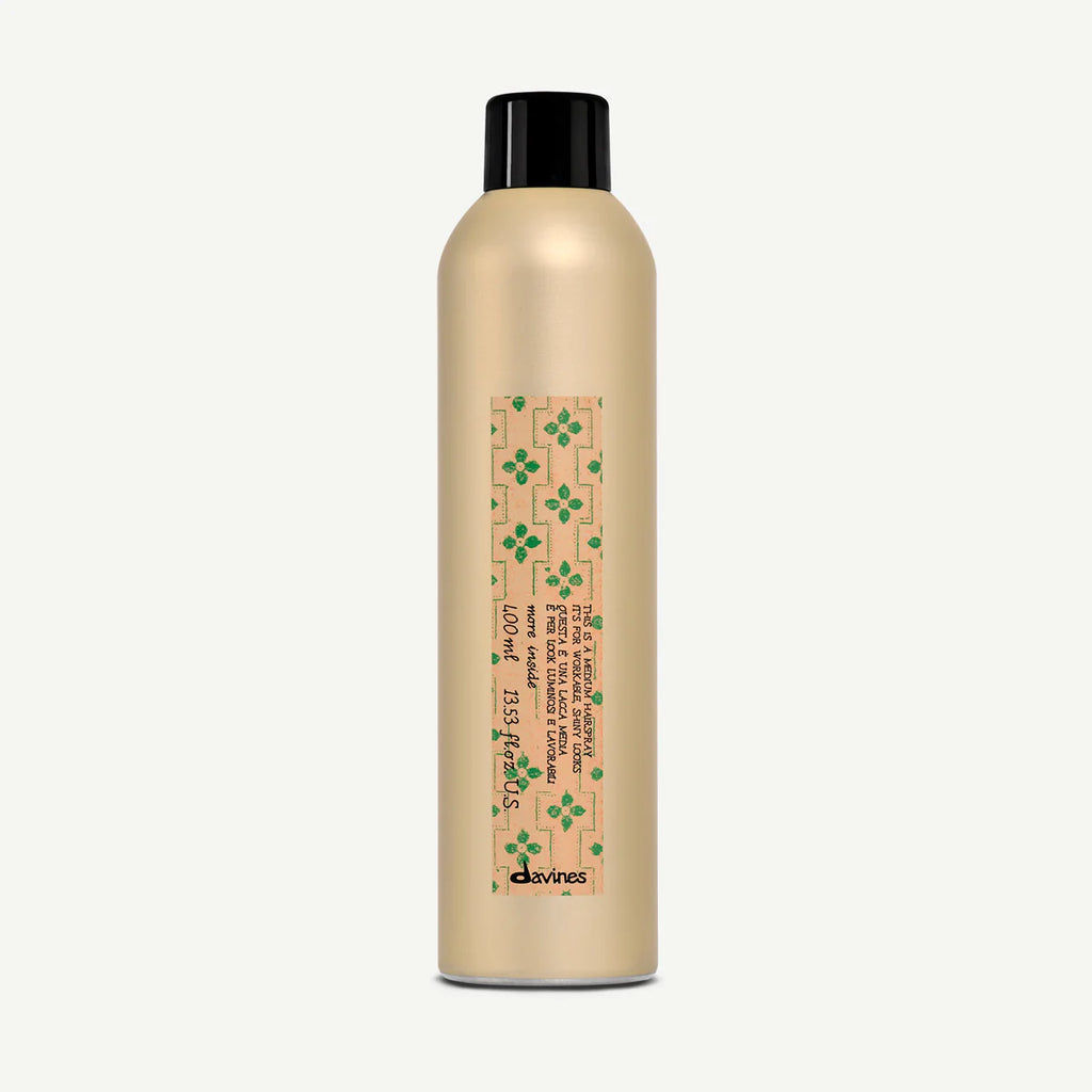 This is a Medium Hairspray i guldig sprayflaska med svart lock och dekorativ etikett med gröna blommor, perfekt för hållbar styling.