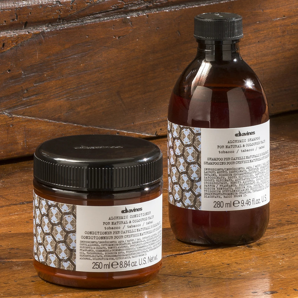 Alchemic Conditioner Tobacco i brunt förpackning med svart lock, miljövänligt balsam för hårvård från Davines, placerad på träbord.