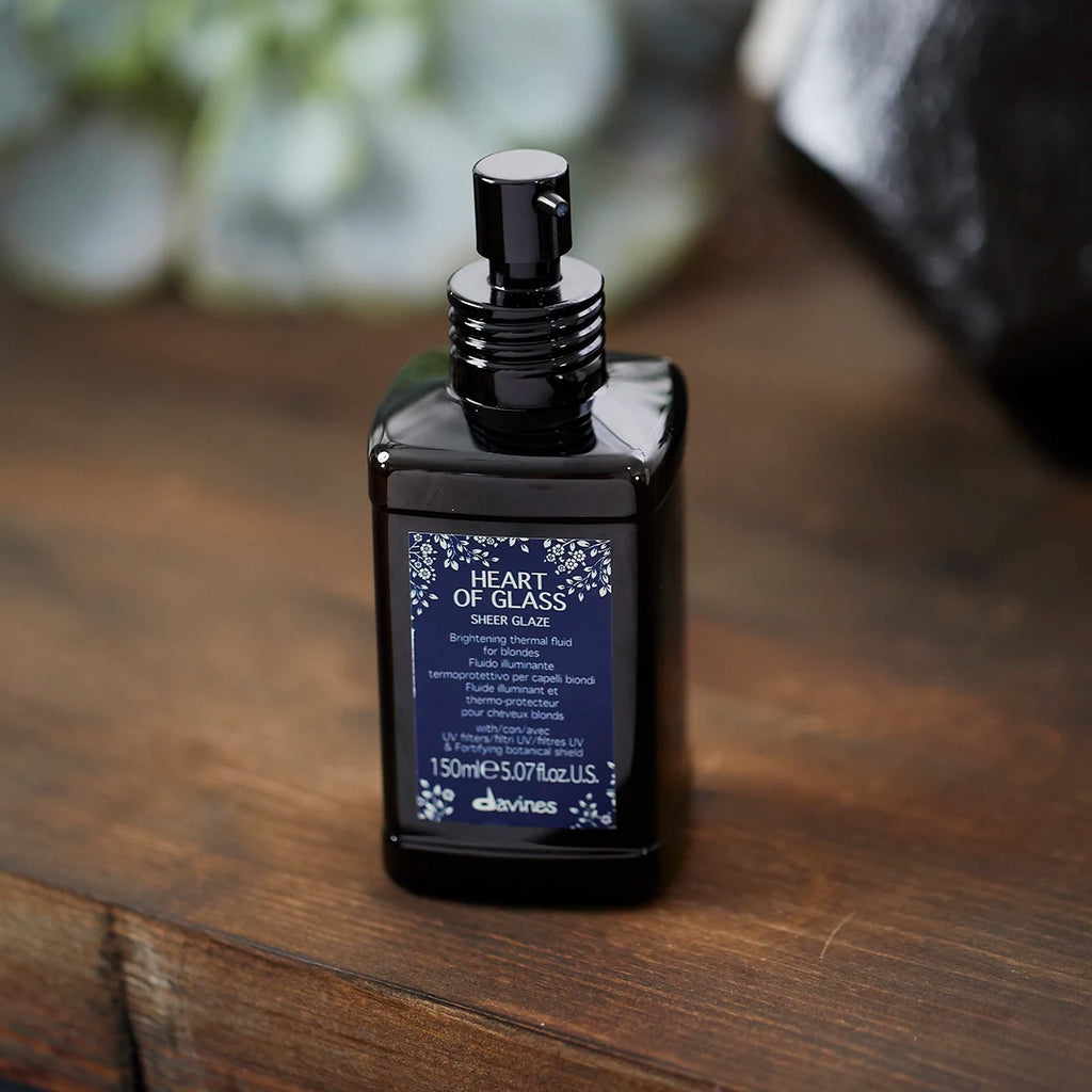 Mörk glasflaska med pump som innehåller Heart of Glass Sheer Glaze, en vårdande och glansgivande hårprodukt för blekt och ljusfärgat hår.
