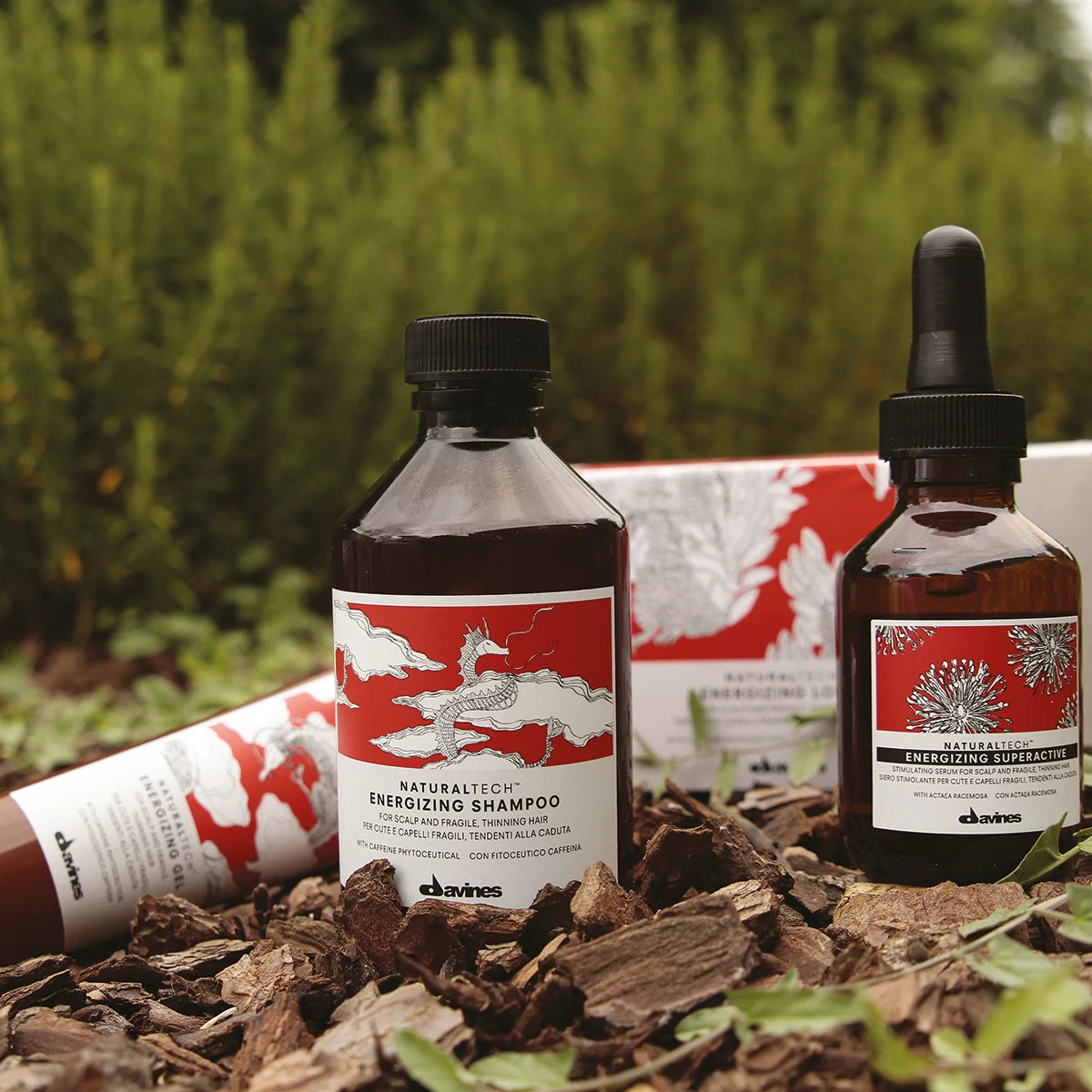 Naturlig hårvårdsprodukt i brun flaska med röd och vit etikett, Naturaltech Energizing Gel, stående på marken bland löv och grönska.