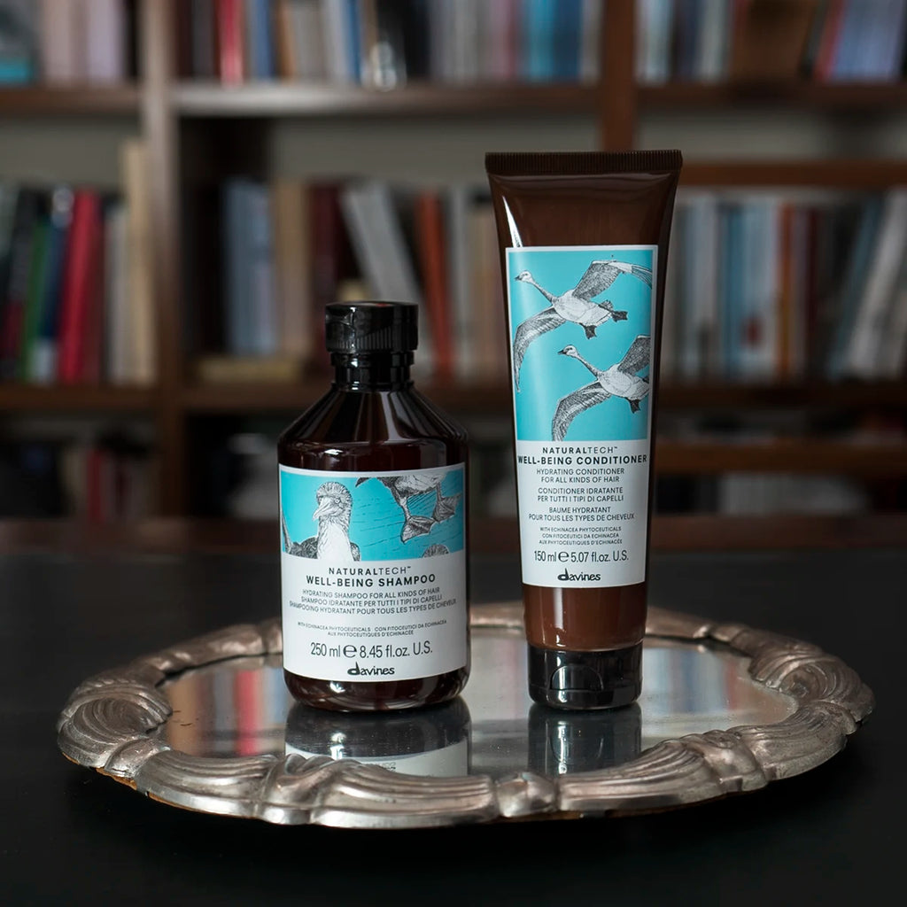 Naturaltech Well-Being Shampoo tillsammans med balsam på en silverbricka, miljövänliga hårvårdsprodukter från Davines med skonsam vård för hår och hårbotten.