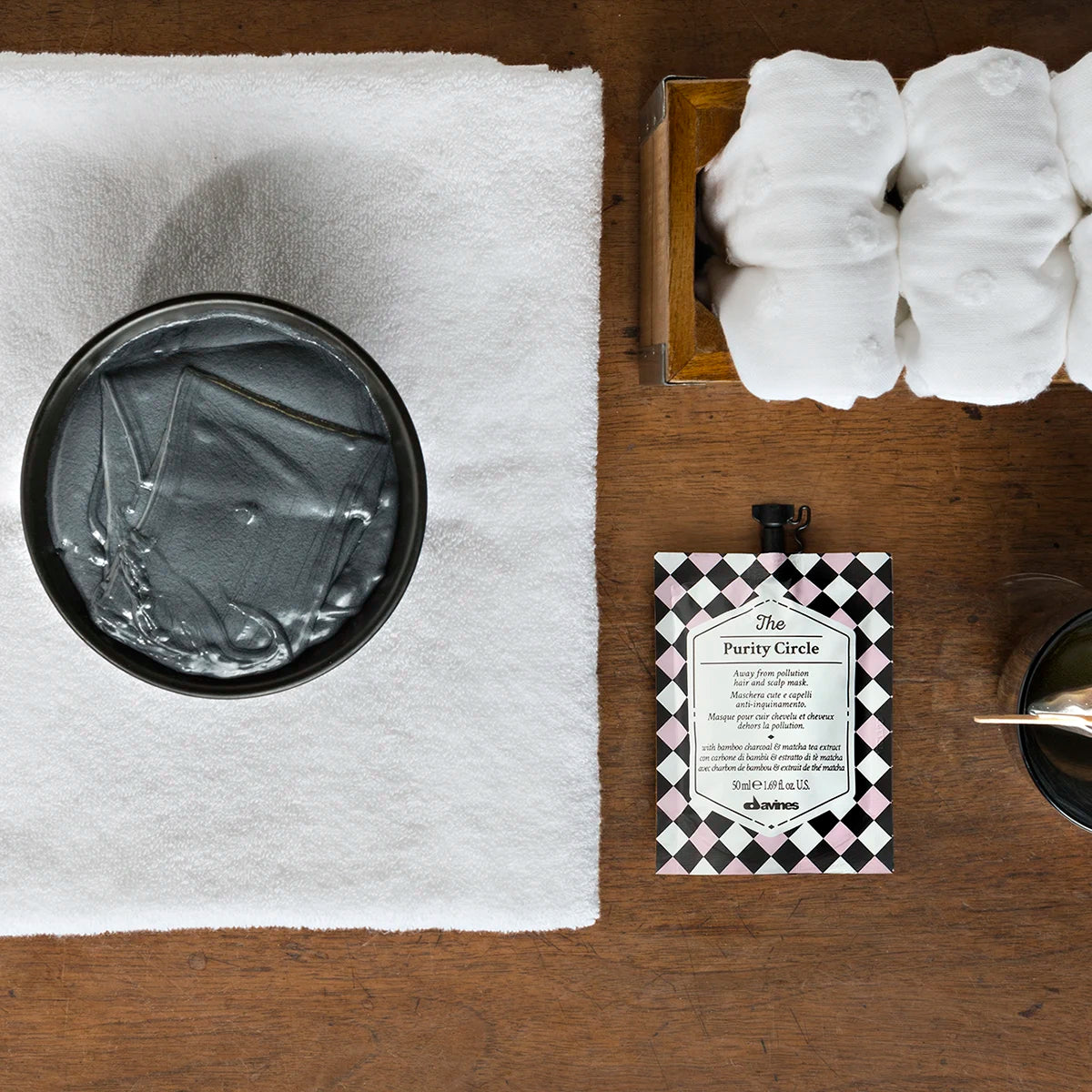 The Purity Circle förpackning bredvid en svart skål med genomskinlig produktgelé på en vit handduk tillsammans med skum och ett urval av hårvårdsprodukter för styling och vård.