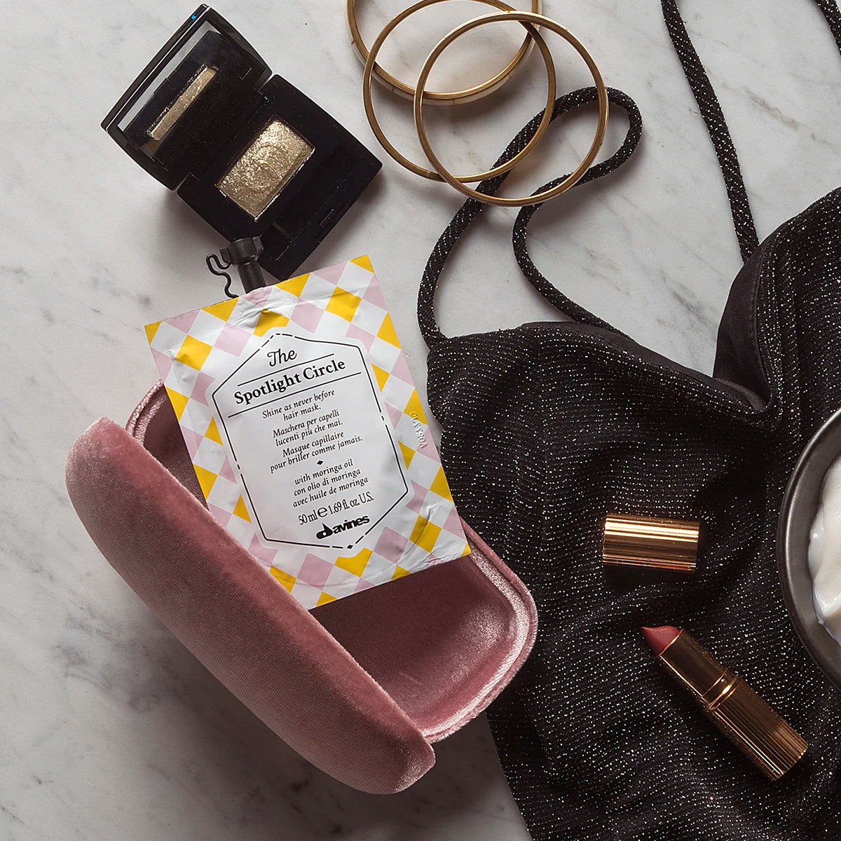 The Spotlight Circle-fuktgivande hårinpackning i en dekorativ förpackning placerad på en rosa etui med lyxiga accessoarer runt omkring på en marmoryta.