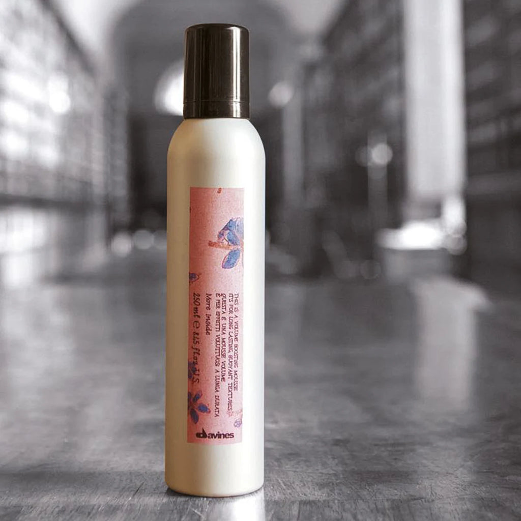 Flaska med This is a Volume Boosting Mousse stylingsprodukt för att ge volym och fyllighet till håret, placerad på en mörk yta.